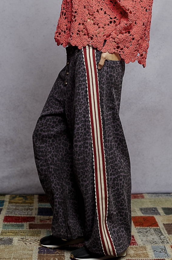 Person wearing a pink lace top and patterned pants with a stripe on a textured floor.