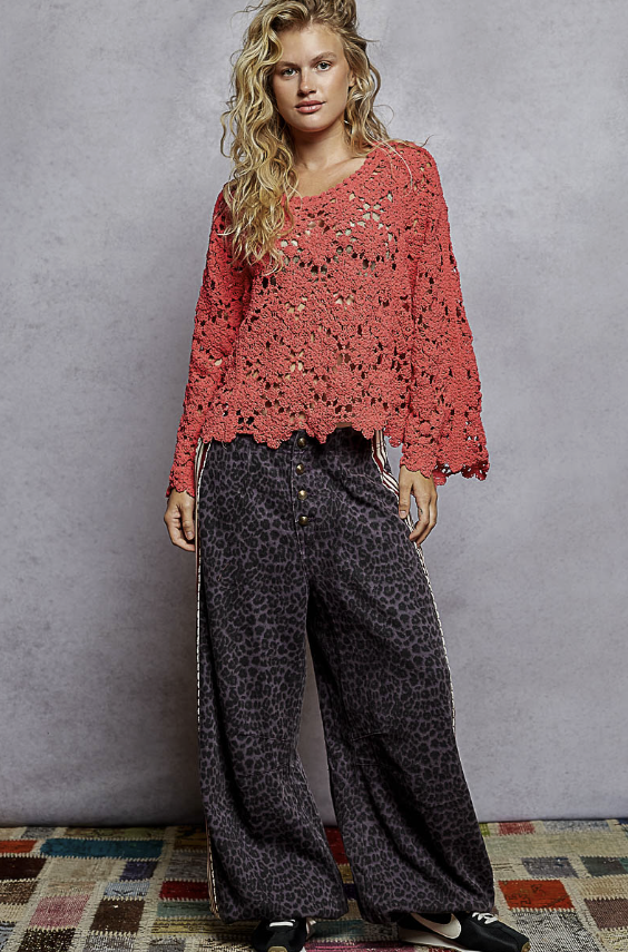 Woman wearing a red lace top and patterned pants against a gray wall.