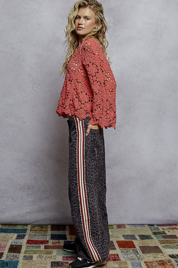 Woman wearing a pink crochet top and patterned pants against a textured wall.