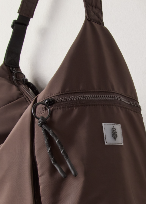 Brown tote bag with zipper and logo on side on plain background