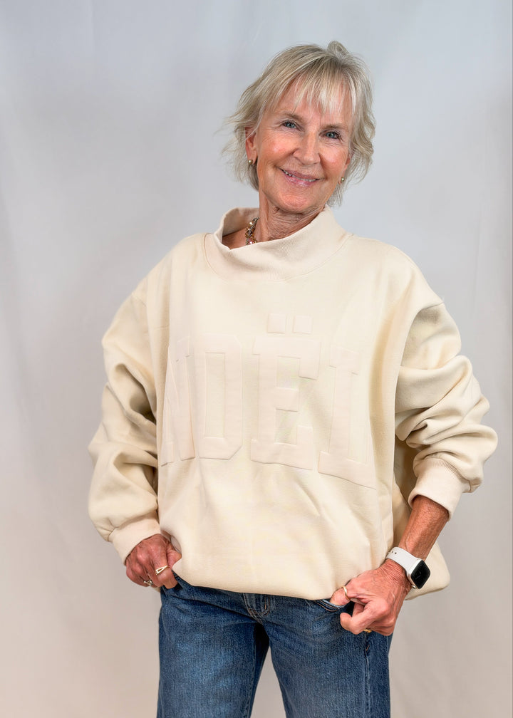 Woman wearing cream color mock neck sweatshirt with &