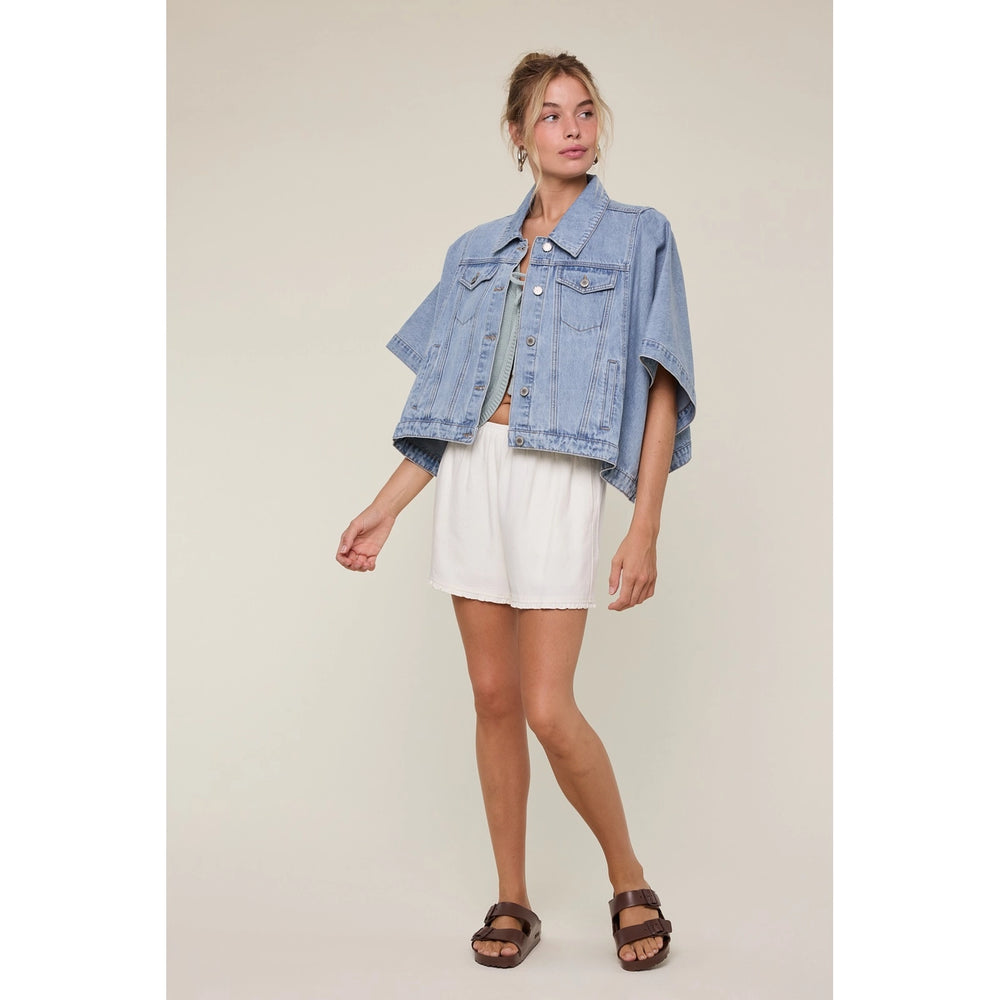 Woman wearing denim cape jacket and white bottoms on plain background