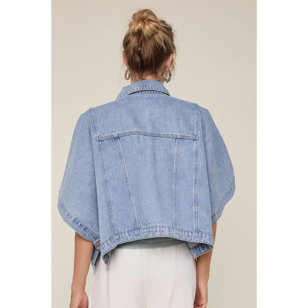 Woman wearing denim cape jacket with white bottoms on plain background