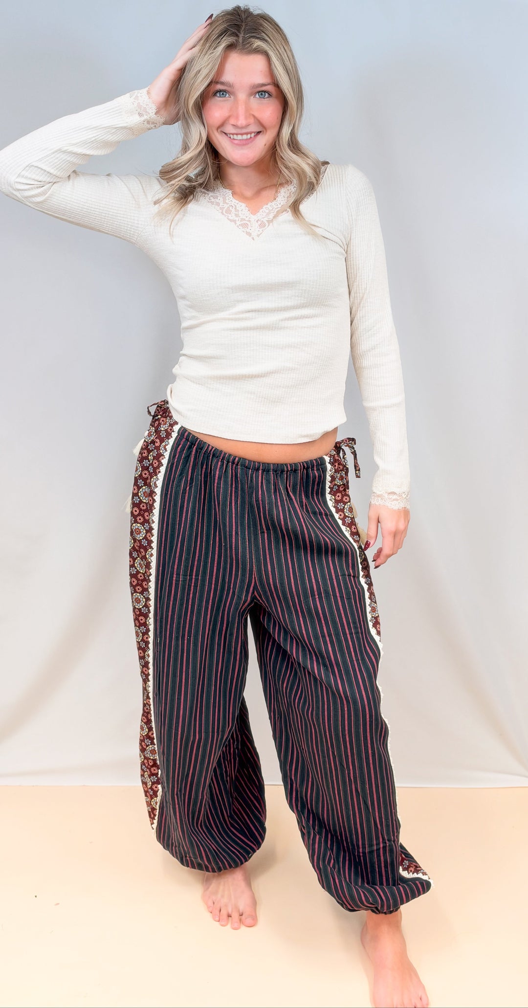 Woman wearing beige lace detail top with black, green and rose color stripe balloon pants on plain background