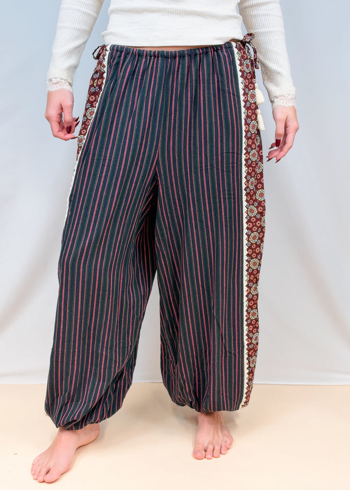 Woman shown from waist down wearing black, green, and rose color stripe balloon pants on plain background