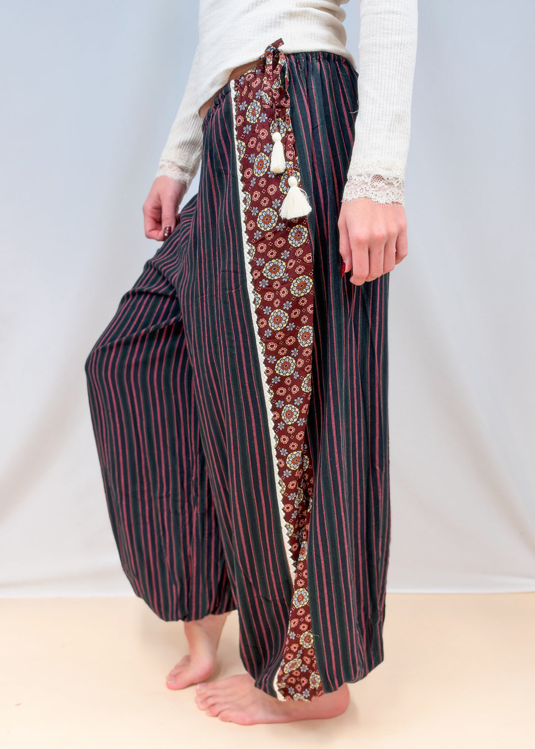 Woman shown from side view wearing black, green and rose color pin stripe balloon pants on plain background