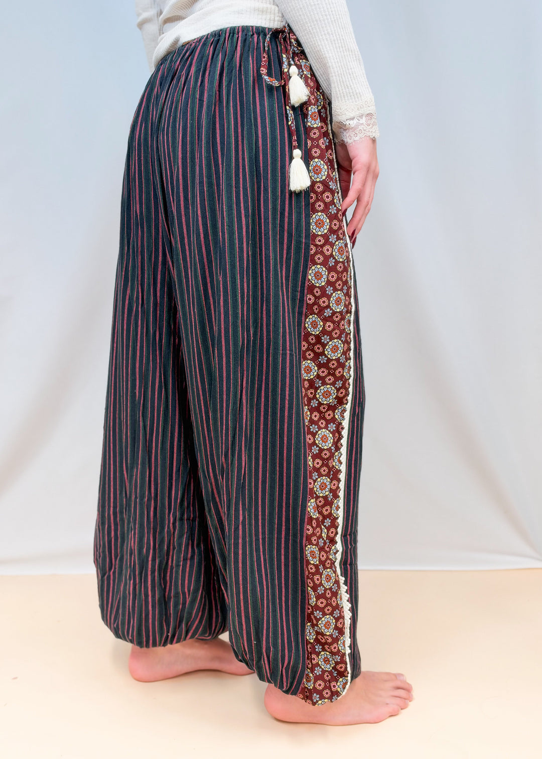 Woman shown from side view wearing black, green and rose color pin stripe balloon pants on plain background