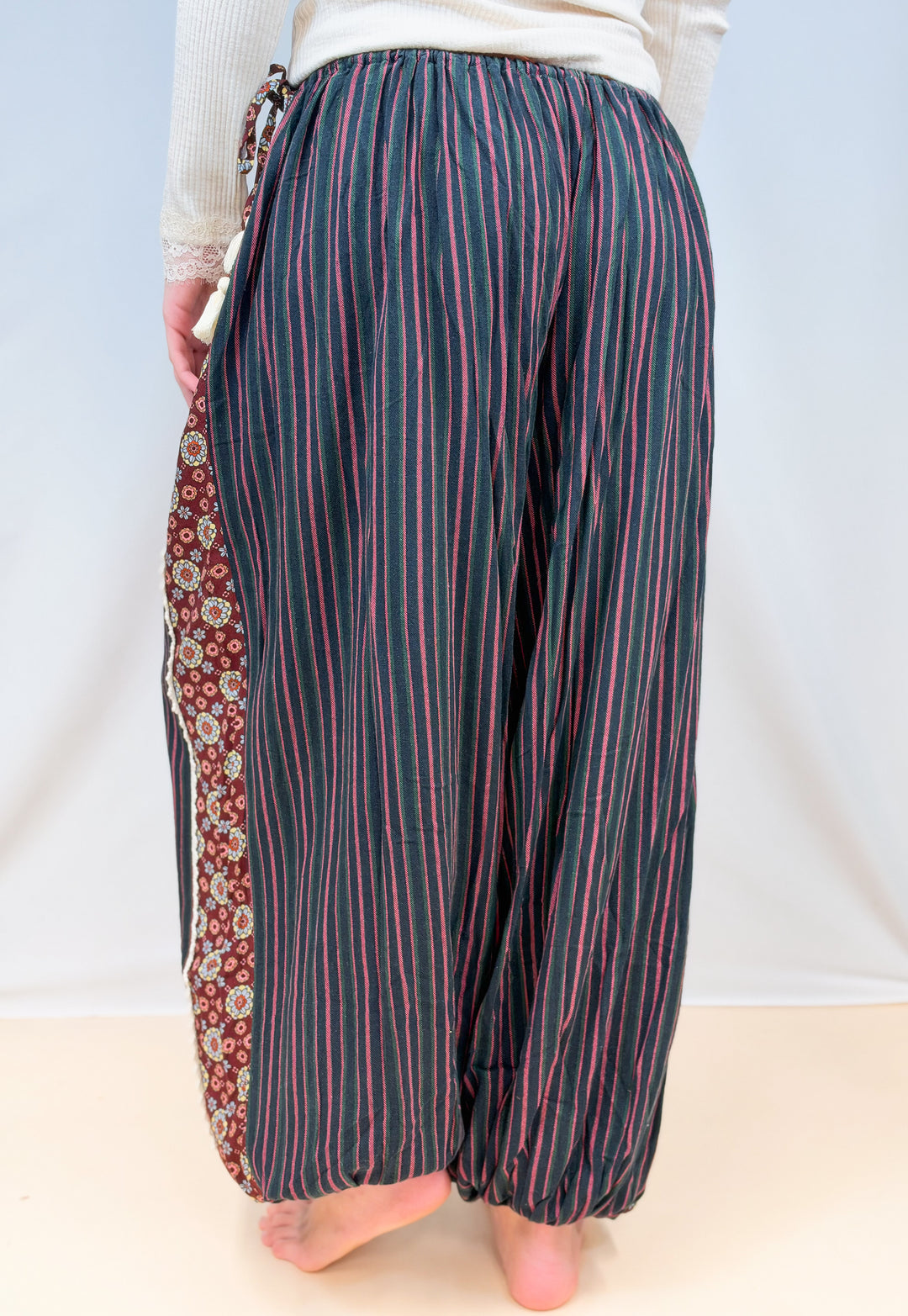 Woman shown from back view wearing black, green and rose color pin stripe balloon pants on plain background