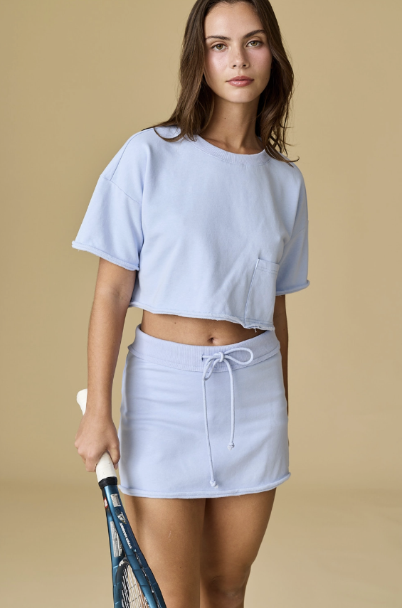 Woman wearing a light blue crop top and skirt holding a tennis racket on a beige background