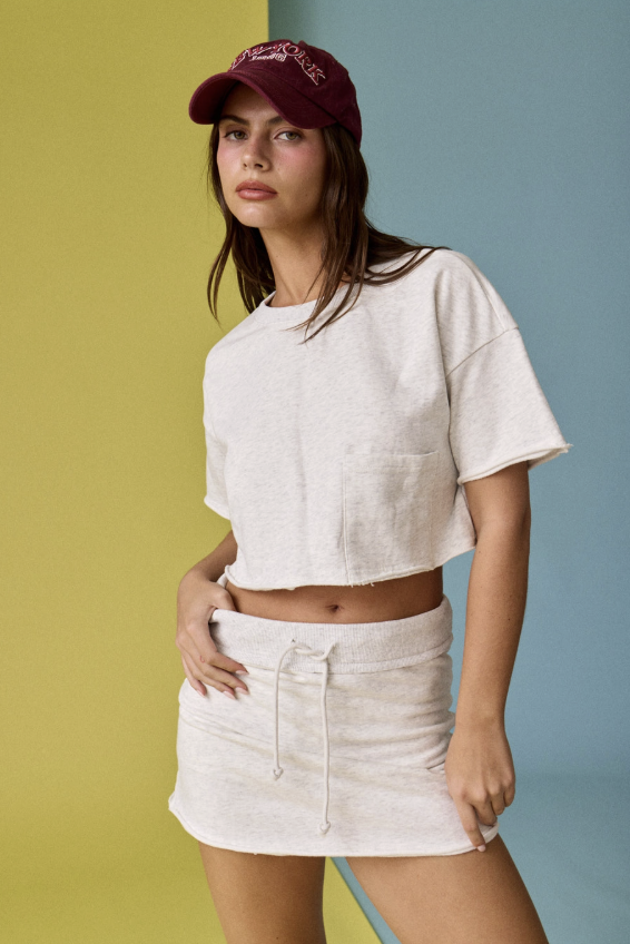Woman wearing a white crop top and skirt with a maroon cap against a multicolored background