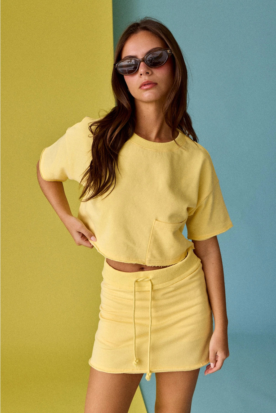 Woman wearing a yellow outfit with sunglasses against a multicolored background