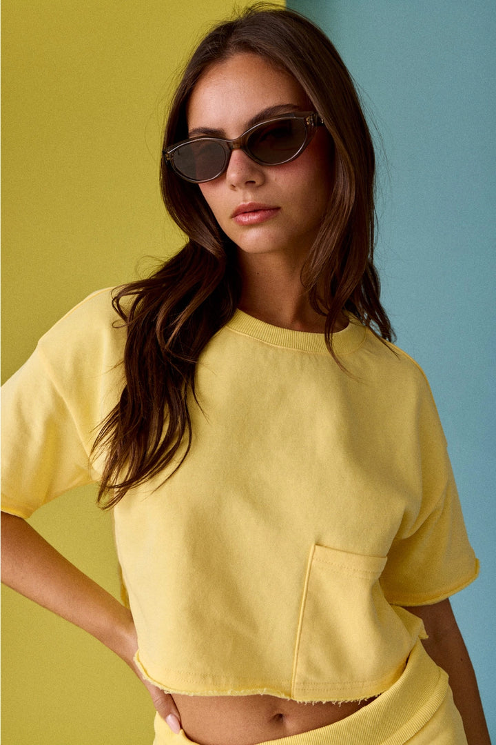 Woman wearing a yellow crop top and sunglasses against a multicolored background