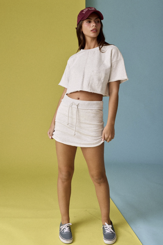 Woman wearing a white crop top and skirt with a maroon cap against a multicolored background
