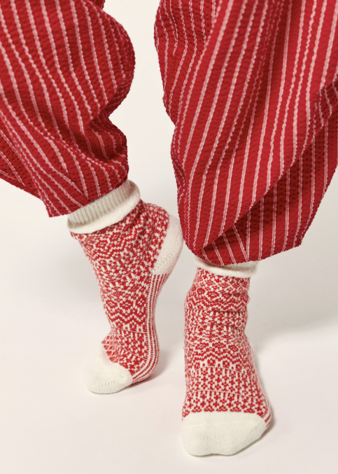 Woman wearing red and white stripe pants with red and cream nordic design socks on cream background