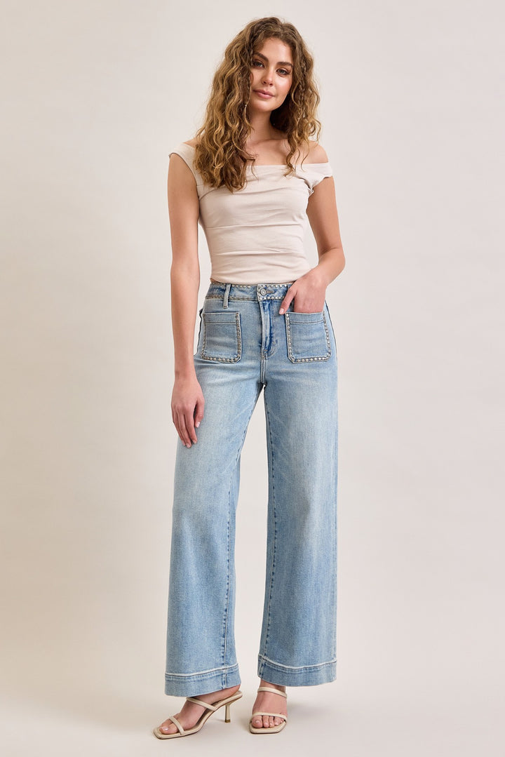 Woman wearing light blue jeans and a beige top on a plain background