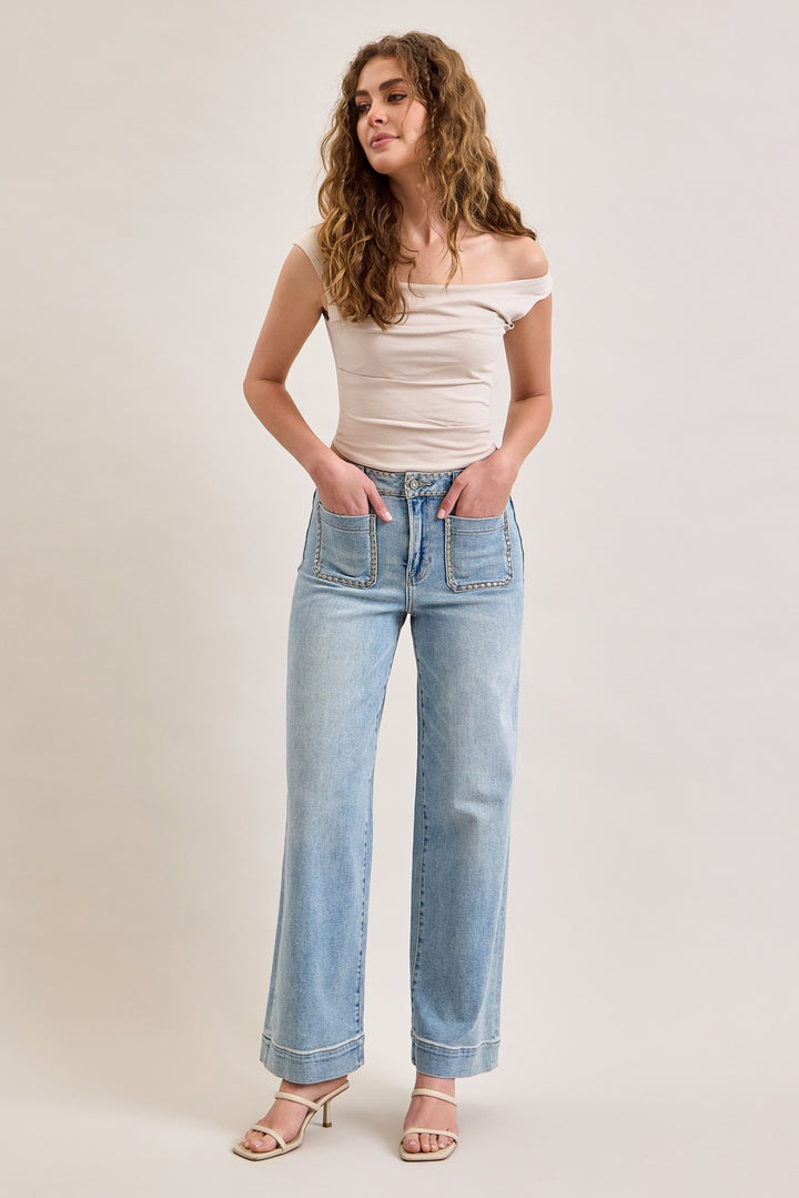 Woman wearing a beige off-shoulder top and light blue jeans on a plain background