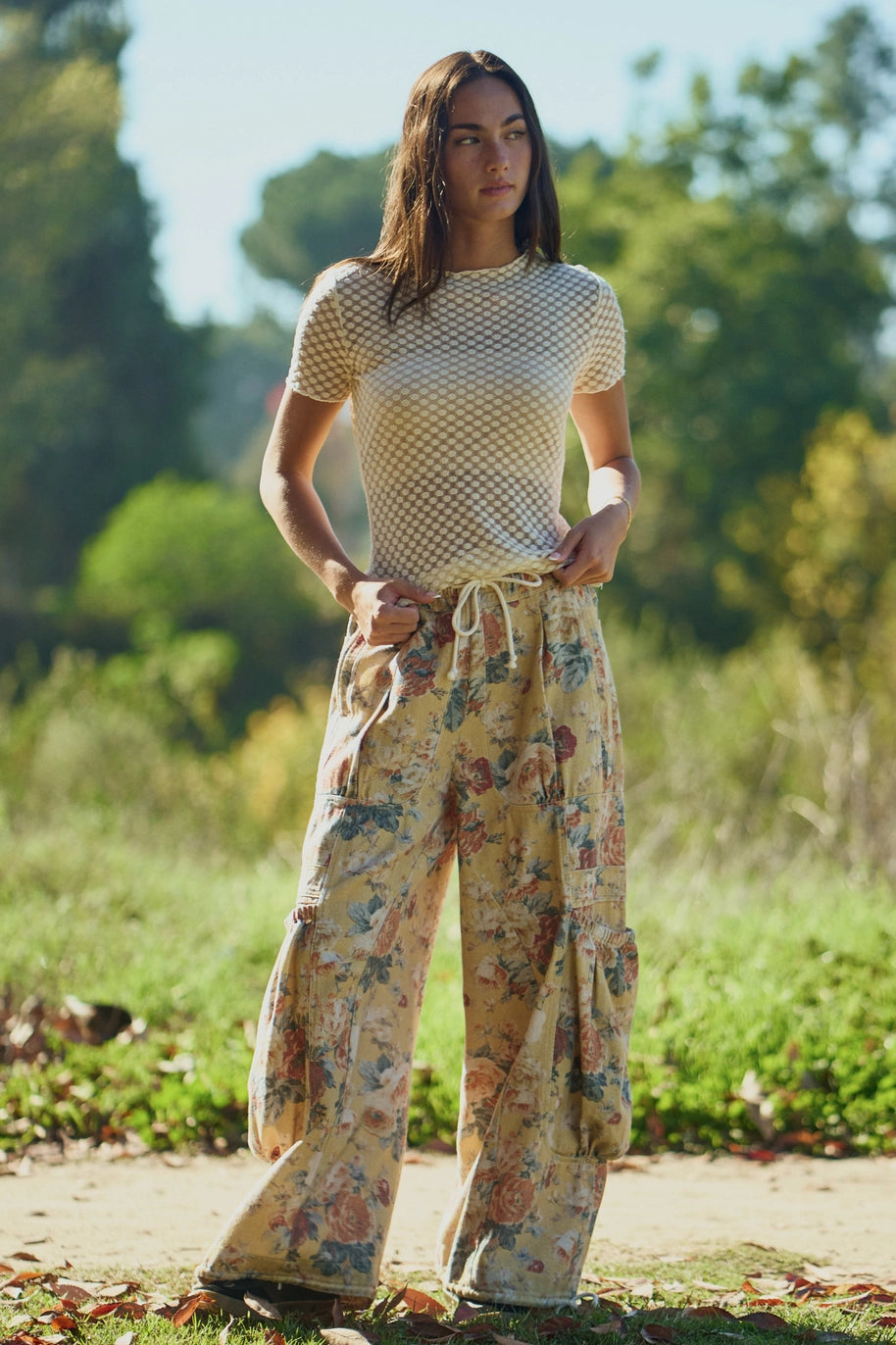 Woman wearing floral pants and beige top standing outdoors