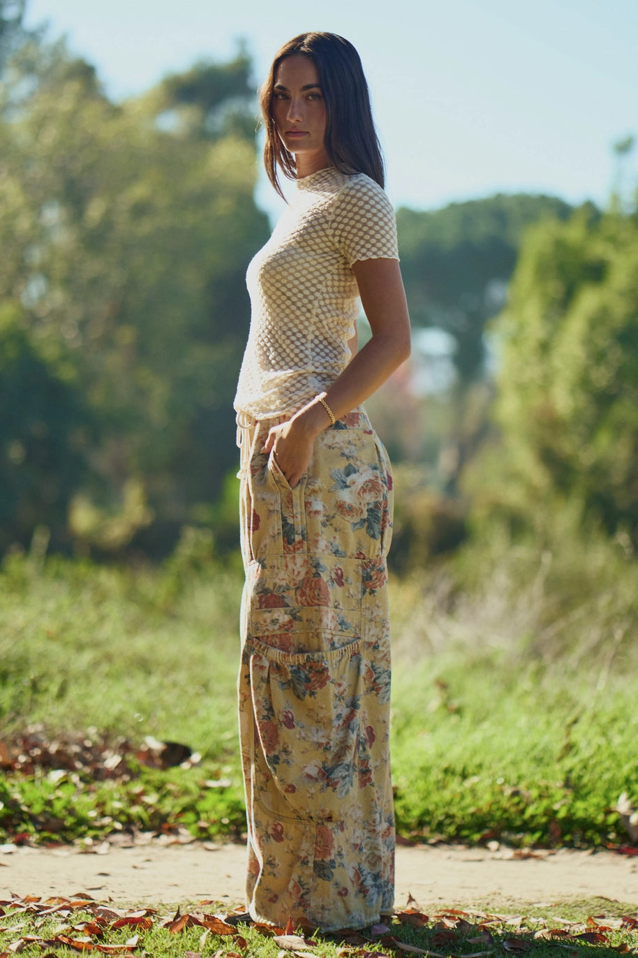 Woman wearing patterned pants standing in a natural setting with trees and grass.