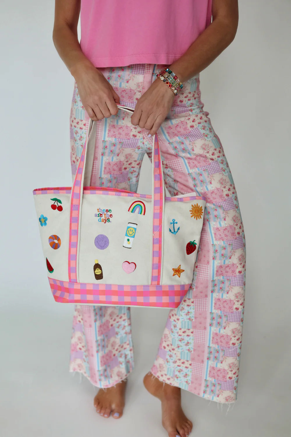 Person holding a tote bag with various embroidered designs against a plain background