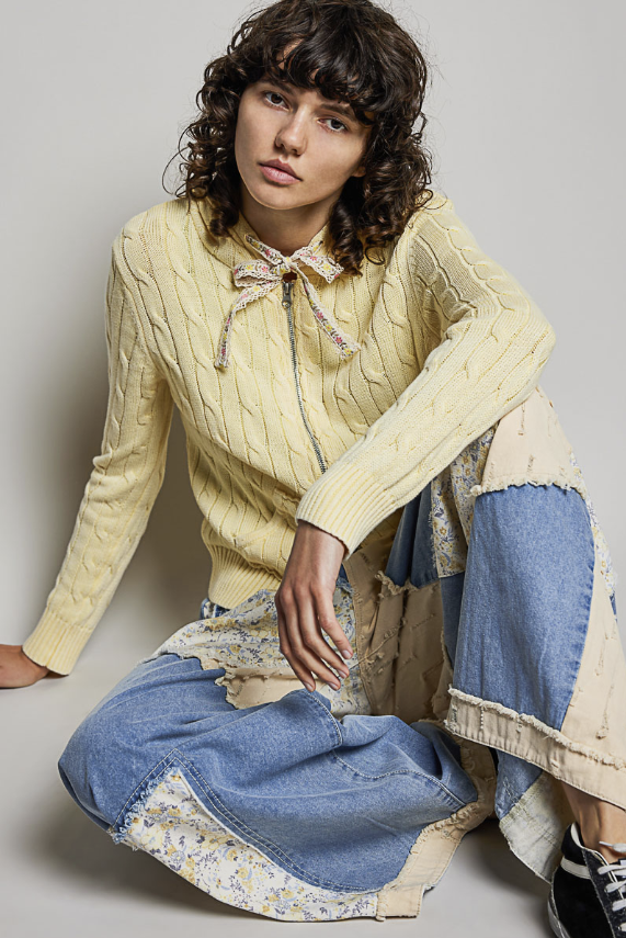 Woman wearing yellow cable knit sweater on plain background