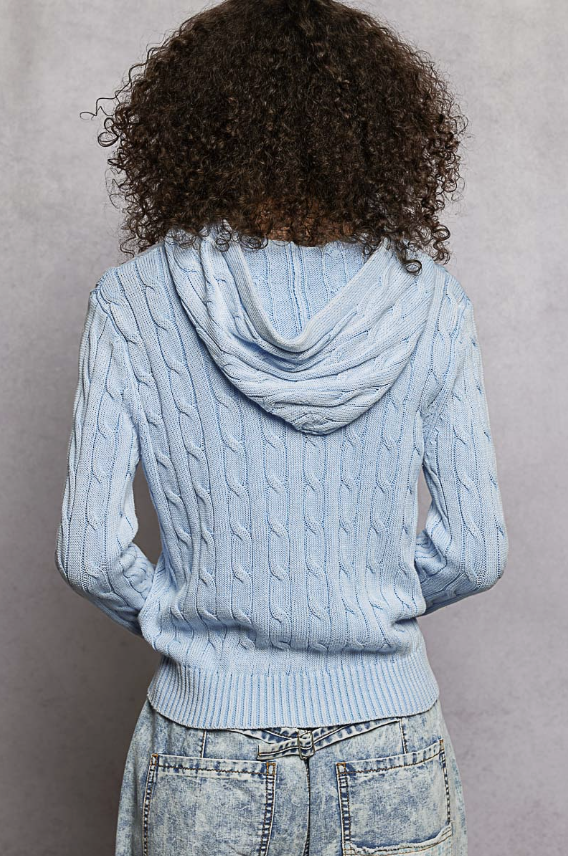 Person wearing a light blue cable knit hoodie against a gray background