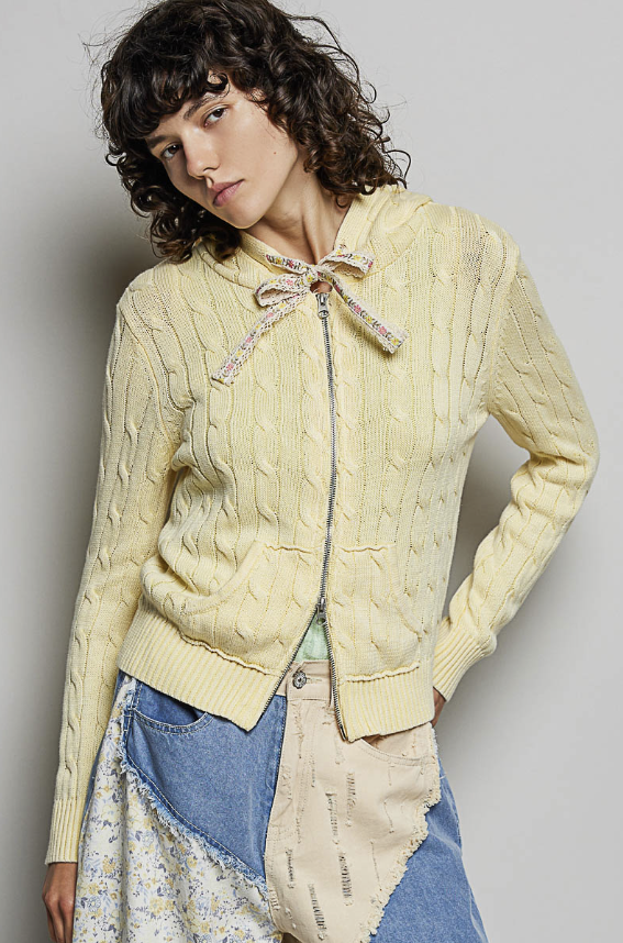 Woman wearing yellow cable knit sweater on plain background