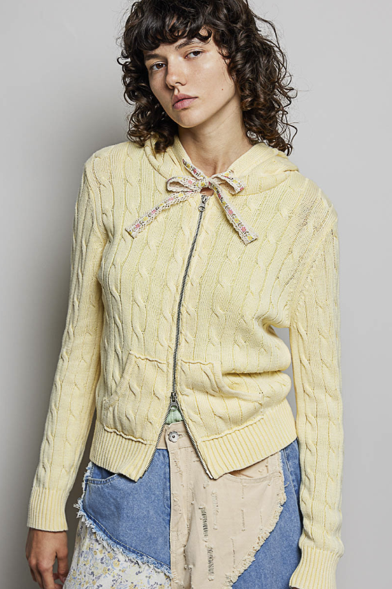 Woman wearing yellow cable knit sweater on plain background