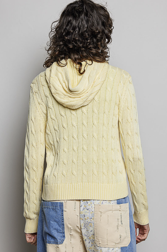 Woman wearing yellow cable knit sweater on plain background