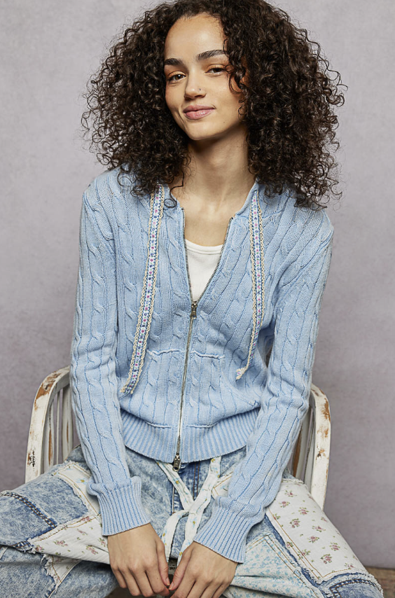 Woman wearing light blue cable knit sweater on plain background