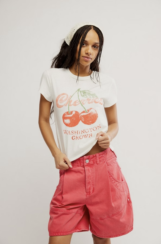 Woman wearing graphic tee with cherries and red shorts on white background