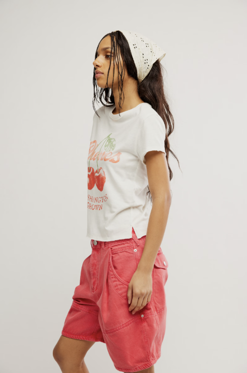Woman wearing graphic tee with cherries and red shorts on white background