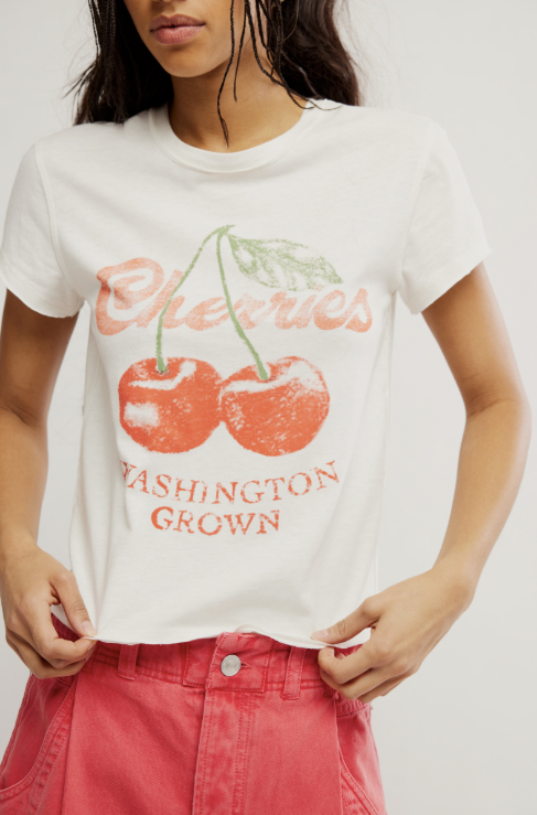 Woman wearing graphic tee with cherries and red shorts on white background