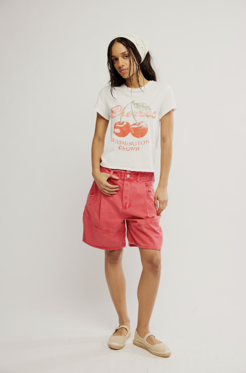 Woman wearing graphic tee with cherries and red shorts on white background