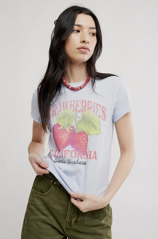 Woman wearing graphic tee with strawberries and green pants on white background