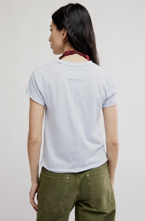 Back of woman wearing blue graphic tee and green pants on white background