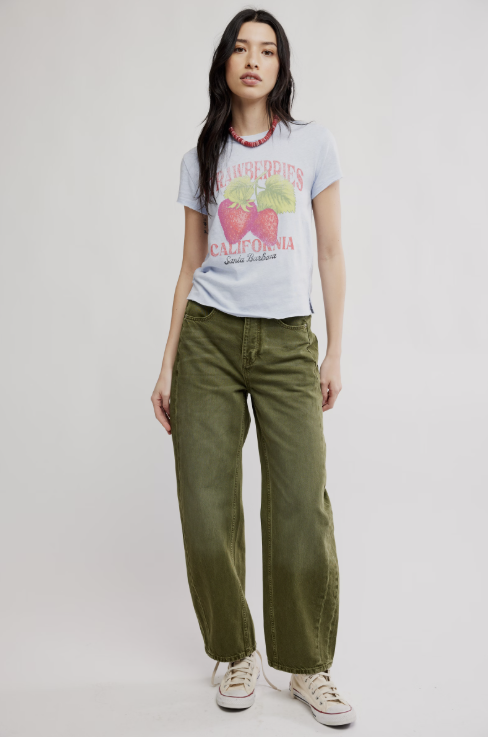 Woman wearing graphic tee with strawberries and green pants on white background