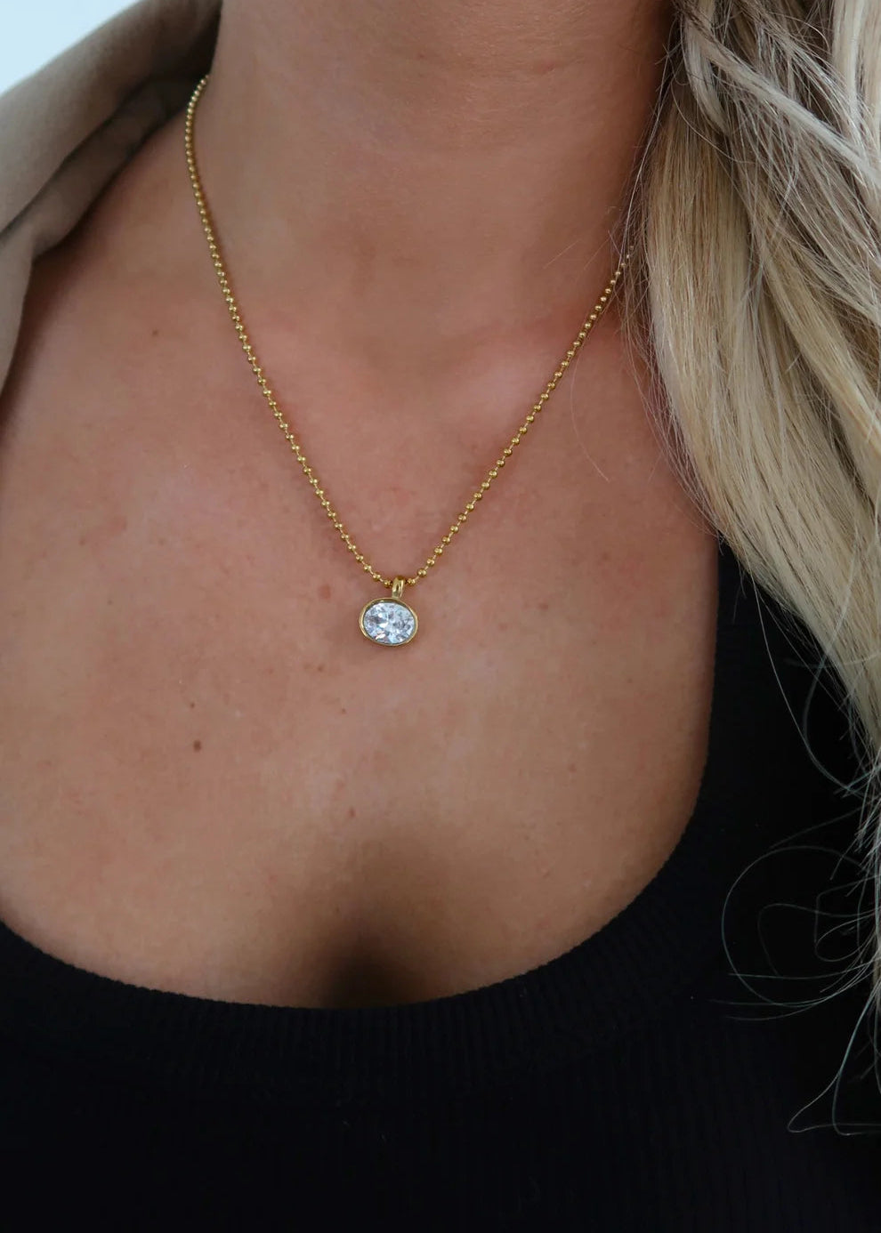 Close up of woman wearing gold ball chain necklace with bezel set oval diamond 