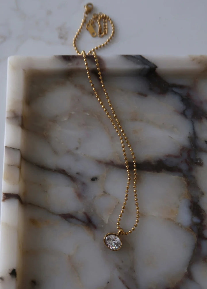 Gold necklace with a small pendant on a marble surface