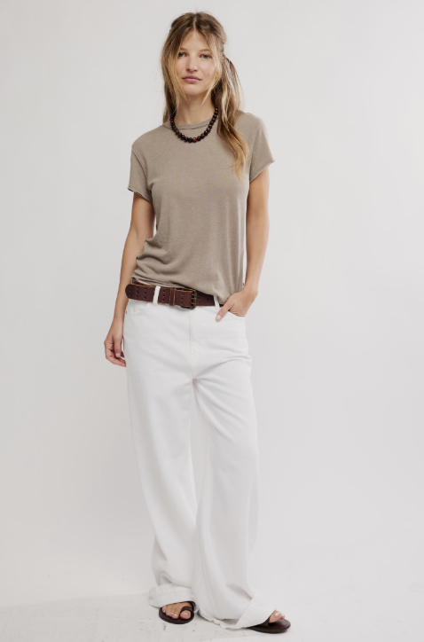 A woman modeling a taupe short-sleeve t-shirt, white wide-leg pants, a brown belt, and black sandals against a plain white studio background.