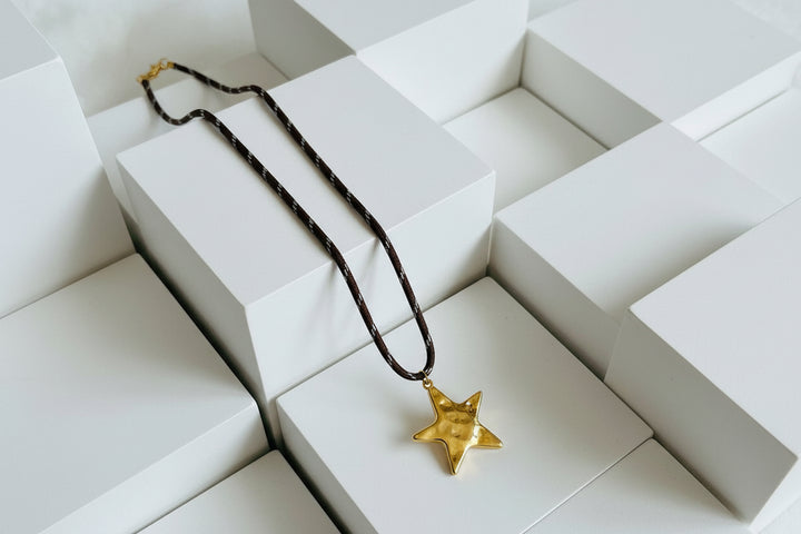 Star-shaped pendant on a brown cord against a white background