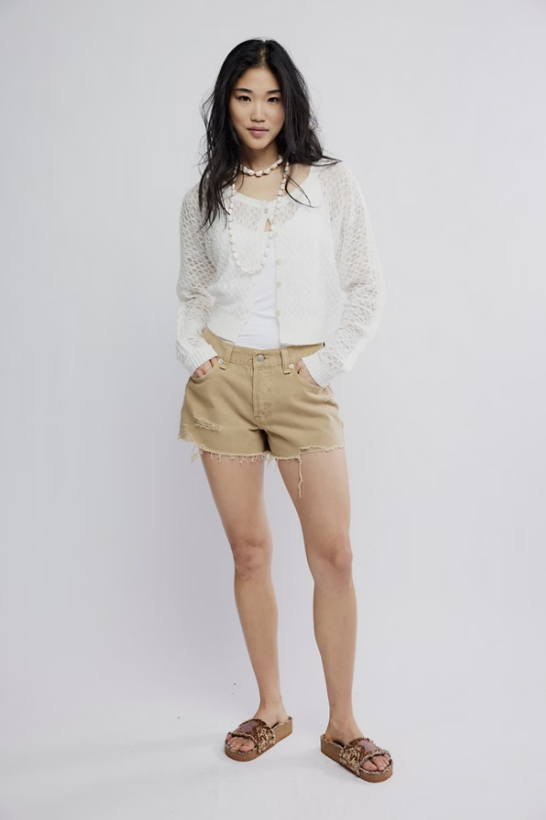 Woman wearing a white lace top and beige shorts on a plain background