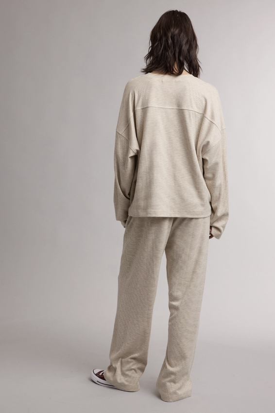 A person shown from the back wearing a matching beige lounge set consisting of a long-sleeve sweatshirt and wide-leg sweatpants, photographed against a neutral light gray studio background.