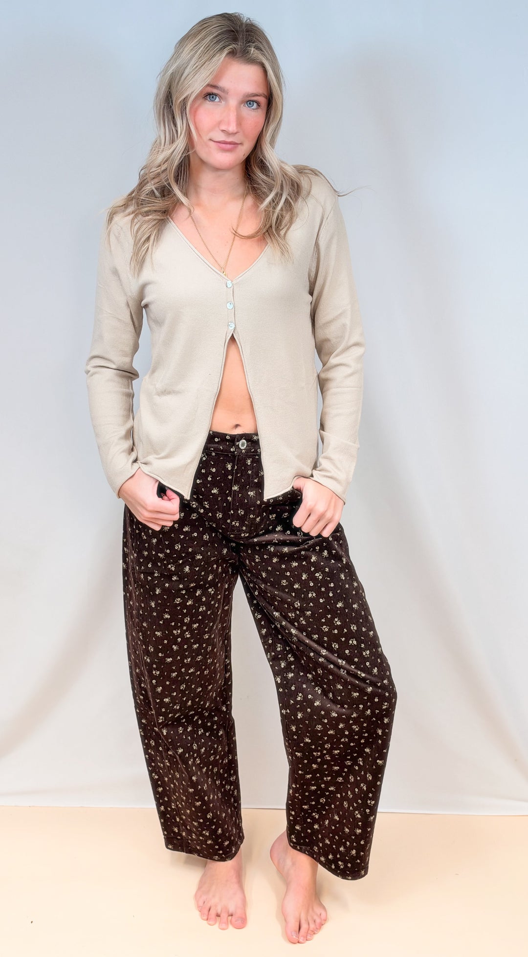 Woman wearing 3 button cardigan with brown corduroy pants on plain background
