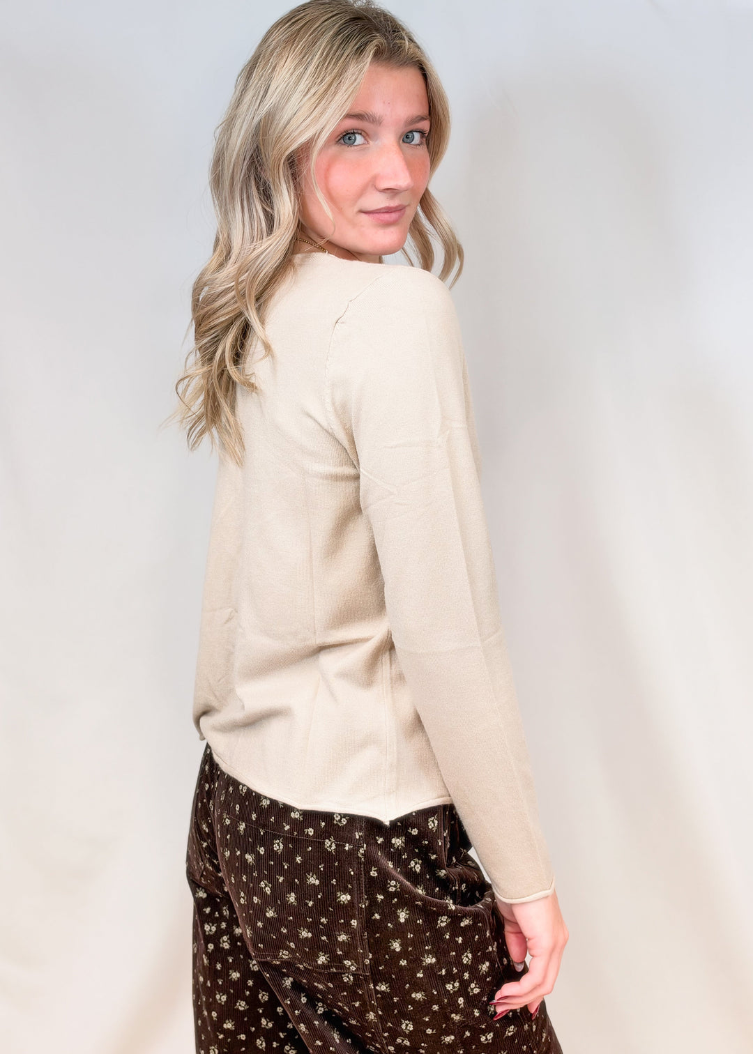 Woman shown from side view wearing oat colored cardigan with brown floral corduroy pants on plain background