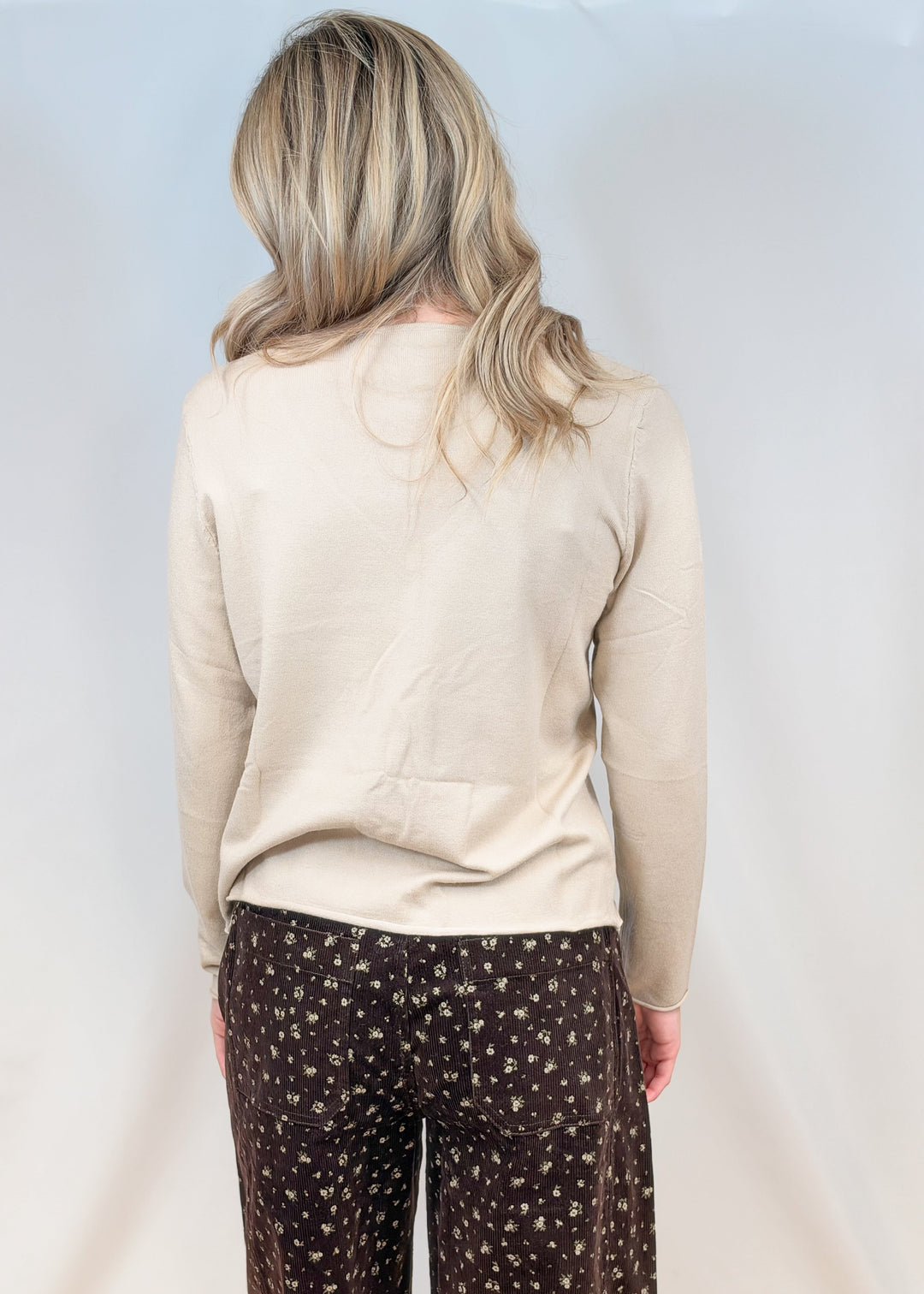 Woman shown from back view wearing oat colored cardigan with brown floral corduroy pants on plain background