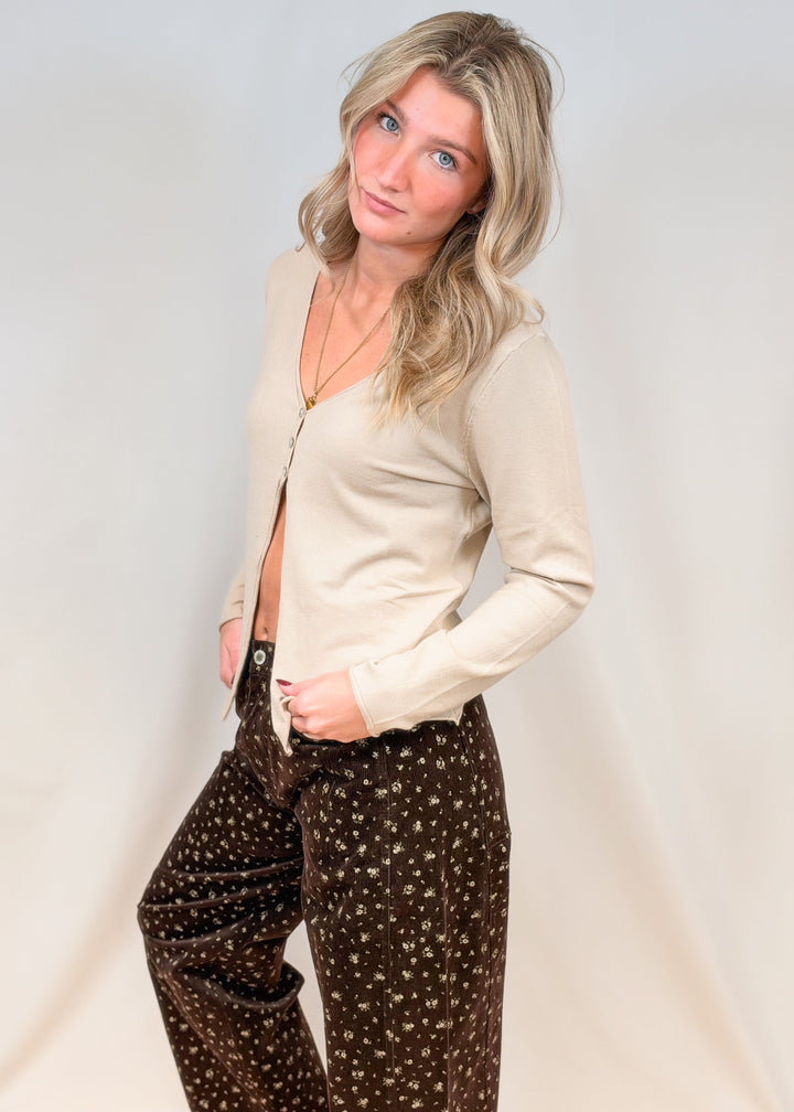 Woman wearing 3 button oat color cardigan with brown floral corduroy pants on plain background