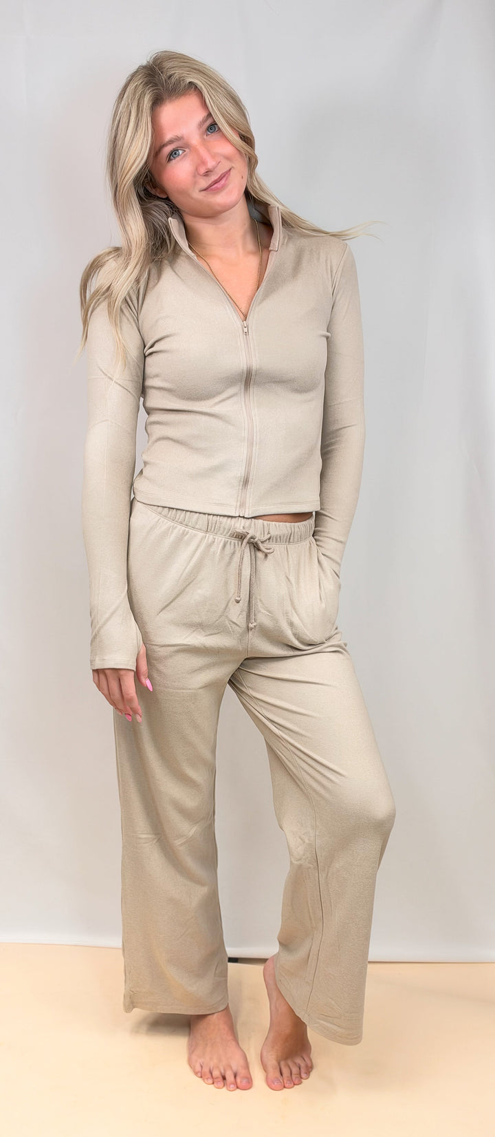 Woman wearing taupe matching set with zip up top and pants on plain background