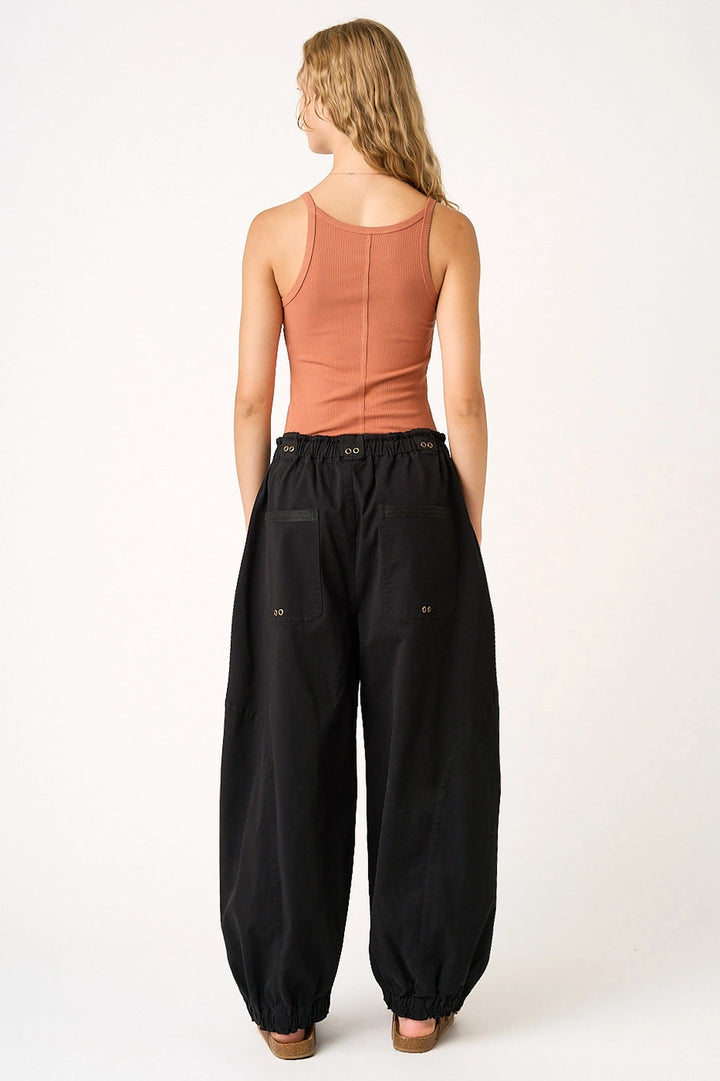 Woman wearing black pants and a peach tank top on a white background