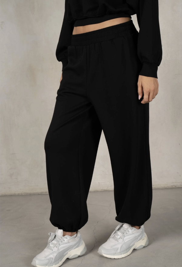 Person wearing black jogger pants and white sneakers against a plain background