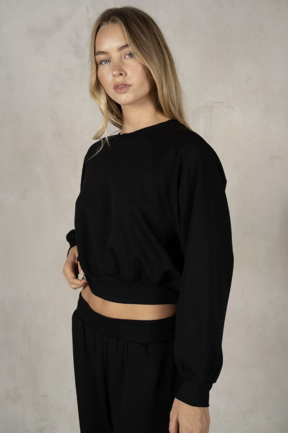 Woman wearing a black sweater and pants against a neutral background